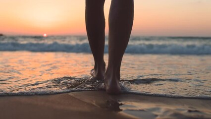 A girl walks barefoot along the beach at sunset, leaving footprints on the sand and reflections in the water. close-up of female legs on the beach. calmness and tranquility. tourist on summer vacation - Powered by Adobe