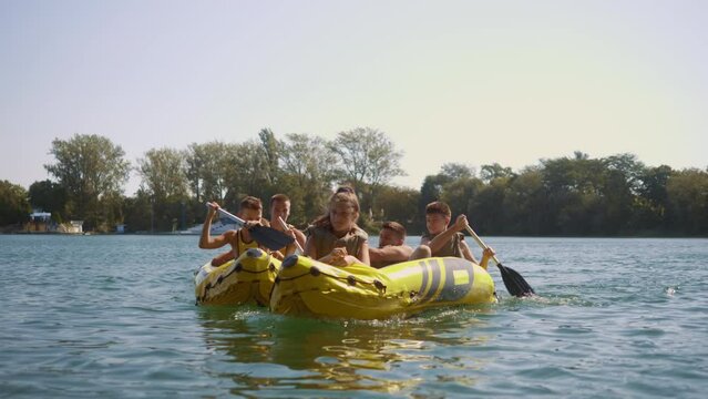 A group of teenagers rowing rubber kayaks on a lake