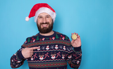 Close-up image of handsome bearded man in santa hat and christmas sweater holding beard balm on...