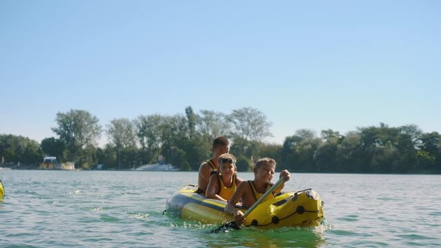 Group of boys are paddling a rubber kayak on a lake