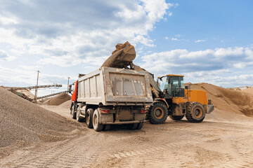 Yellow Excavator loading sand to industrial truck on industry quarry. Construction site open pit mine concept