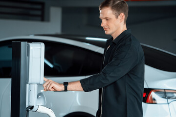 Young man travel with EV electric car to shopping center parking lot charging in downtown city...