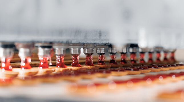 Food industry banner, Red fruit jam squeezed onto cookies biscuit production in modern factory on conveyor belt