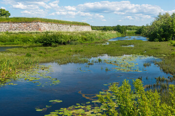 the old medieval fortress walls are overgrown with grass and in front of the walls there is an old overgrown moat with water in places. Novodvinsk fortress near Arkhangelsk