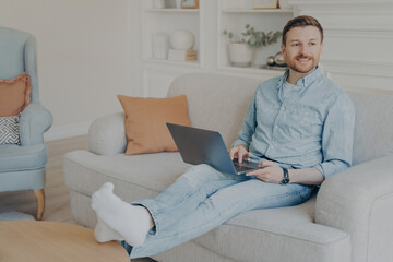 Smiling man working on laptop while sitting comfortably on a sofa in a cozy living room