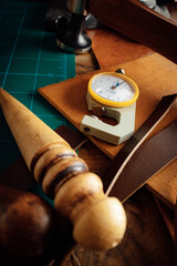 A skilled craftsman captures the essence of time with a precision blade on a weathered cutting mat, surrounded by the rustic charm of his leather-filled studio, while the ticking clock and the camera