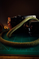 A beautifully crafted leather camera with a handmade strap rests upon a vibrant green surface in...
