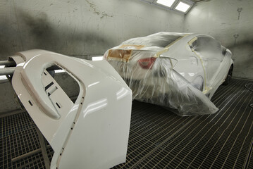 The photograph captures the scene of an automotive workshop, showcasing the process of painting...