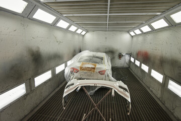The photograph captures the scene of an automotive workshop, showcasing the process of painting...