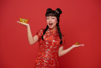 Happy Chinese new year. children asian girl wearing traditional qipao dress holding gold ingot...