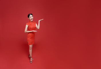Happy Chinese new year. Asian woman wearing traditional cheongsam qipao dress with gesture of welcome isolated on red copy space background.