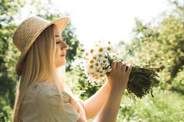 A portrait of a beautiful young woman wearing a straw hat with  flowers on a summer greenery...
