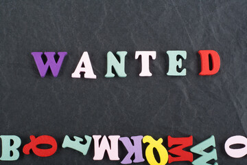 WANTED word on black board background composed from colorful abc alphabet block wooden letters, copy space for ad text. Learning english concept.