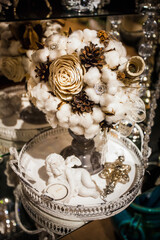 Winter decorative Christmas bouquet of cotton wool, cones, artificial flowers, ribbons and decorations, on an iron tray with a ceramic angel.