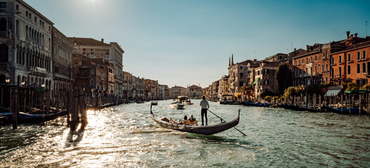 A lively group of travelers glide down the grand canal, surrounded by a bustling cityscape and the...