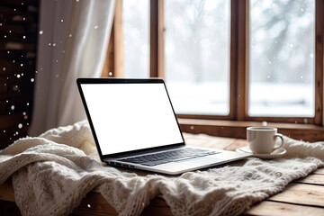 Laptop with a white screen mock up in winter, indoor on the table with a cozy blanket by the window with snow. Seasonal remote work, internet, shopping, Christmas and New Year.