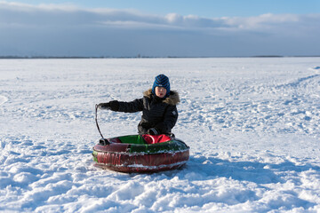 Fototapeta na wymiar child boy riding on snow tubing downhill. Winter joy and outdoor activity