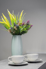 a vase of flowers and 2 white mugs on the table