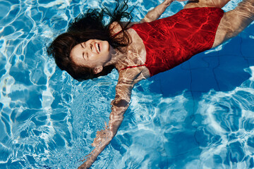 Young woman in the pool in a red swimsuit with a beautiful smile lying on the water and swimming in...