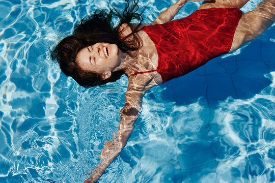 Young woman in the pool in a red swimsuit with a beautiful smile lying on the water and swimming in the sun swimming in the pool, the concept of relaxing on vacation.