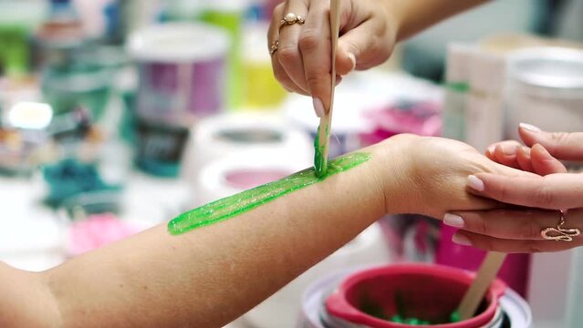 Applying green paste for sugaring with a wooden stick to the female hand of an adult in a beauty salon. The concept of accessibility of sugaring as a method of depilation and hair removal