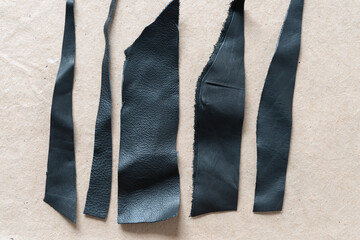 grungy stripes of cut black leather pieces on plain brown paper
