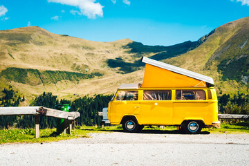 A vibrant yellow van stands still on a winding road, its wheels ready to take on the rugged terrain as the majestic mountains tower above, beckoning the adventurous soul to explore the untamed beauty
