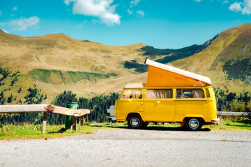 A vibrant yellow van, nestled in the grassy landscape, gazes upon the majestic mountains, its wheels yearning for adventure and transport to new horizons