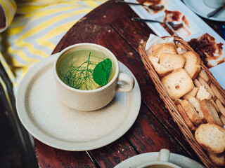 A steaming bowl of hearty soup accompanied by crisp crackers sits on a rustic wooden table, surrounded by vibrant green kitchenware, creating the perfect comforting brunch meal for a cozy indoor afte