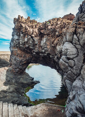 A majestic cloud-framed arch carved by nature's erosion, bridging the serene waters below, stands as a testament to the enduring power of geology and the beauty of the wild outdoors