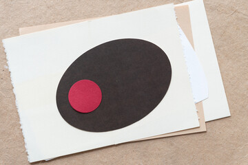 red paper circle on dark brown paper oval both on a pile of vintage paper sheets on plain brown...