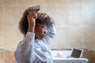 Young African American woman combing her hair with a black comb in a home room