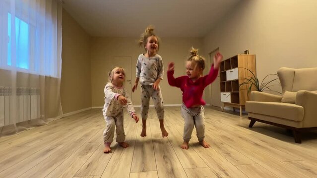 little triplets sisters are running wild and playing in a large room, they are wearing pajamas, they are running, jumping, fighting and laughing