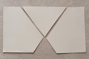 beige stationery sheet cut into three pieces on plain brown paper