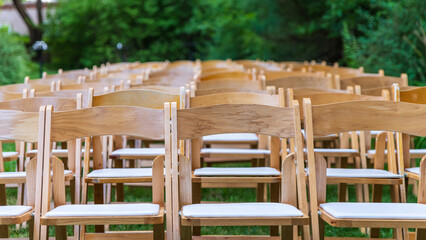 Wooden folding chairs in a garden before an outdoor wedding ceremony.