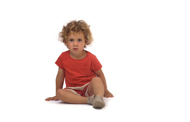 front view of a boy dressed in summer clothes sitting on group and looking at camera on white background (3 year old)