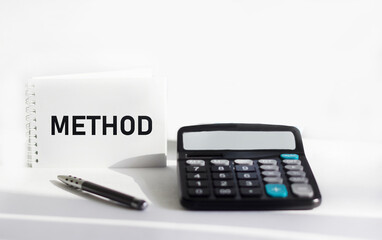 Notepad with the text Method lies on a white background with a calculator. Financial concept