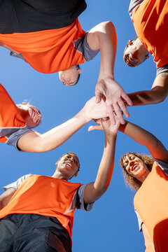 Looking up at a team of female soccer players. The women are joined in unity and cheering before a match. 