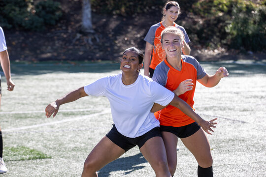 Female soccer players play in an intense and competitive game on the field outside. 