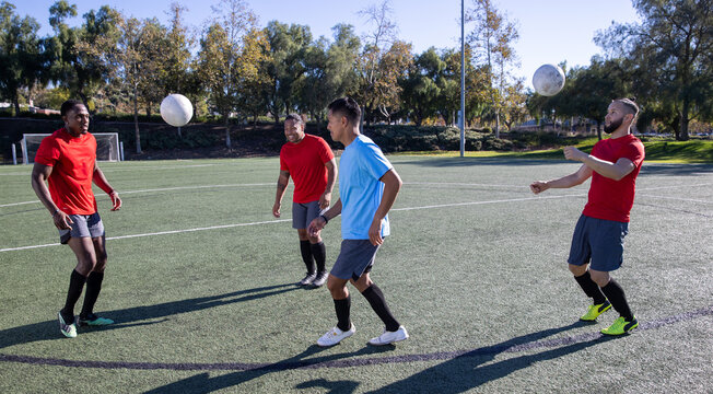 Soccer players work together as a team playing the game together. The men are having fun at practice on the field. 