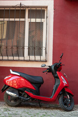 Red motorbike in front of the window of the house.