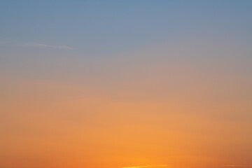 Abstract landscape of a sunset. The evening sky shifts color from orange to dark blue in a smooth gradient, with some faint clouds visible.