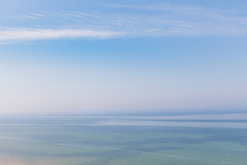 Blue sky with haze and blurry glowing pink clouds above the sea. Shallow coastal sea water with...