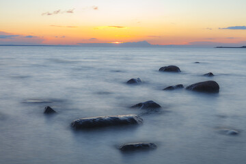 Naklejka premium Evening at the shore of Baltic sea. Bright sunset and sea waves. Erratic boulders. Long exposure.