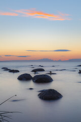Fototapeta na wymiar Evening at the shore of Baltic sea. Bright sunset and sea waves. Erratic boulders. Long exposure.