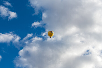 A yellow hot air balloon floats in the air, with white clouds and blue skies.