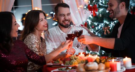 Group of happy people at a table of celebrating in christmastime with glasses with wine and giving gifts to each other