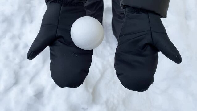 Hands in mittens are throwing the snowball on the white snow background, selective focus. Waiting for snowball fights. Concept of snow game, gadget-free activities for children and parents