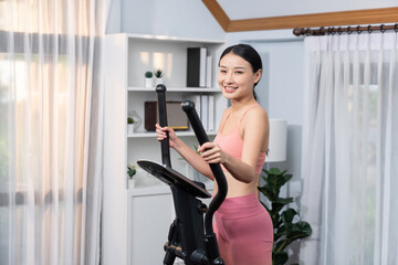Energetic and strong athletic asian woman running on elliptical running machine at home. Pursuit of...