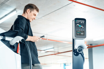 Young man travel with EV electric car to shopping center parking lot charging in downtown city...